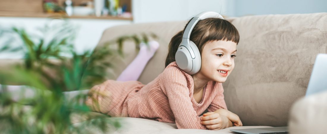 A delightful little girl, aged 5-6 years old, wearing headphones while captivated by the laptop screen. Concept: technology-infused relaxation, online education, computer entertainment