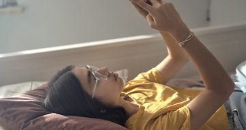 Caucasian teenage girl browsing phone while lying on bed