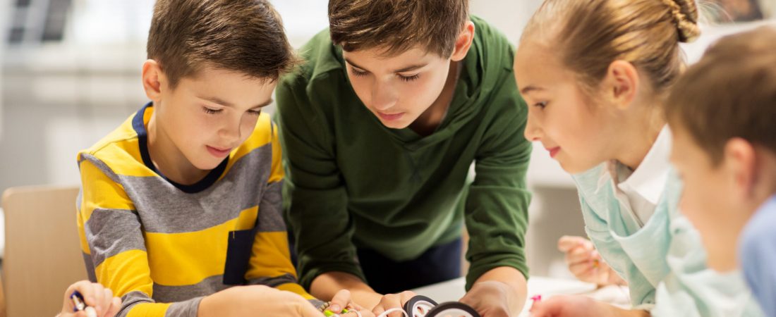 education, children, technology, science and people concept - group of happy kids building robots at robotics school lesson