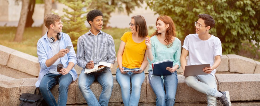 High-School Students Learning Doing Homework Together Using Gadgets Sitting Outside In Park. School Friends Concept