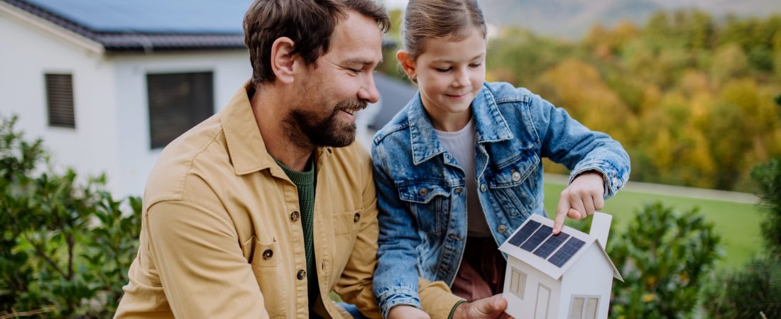 Little girl with her father holding paper model of house with the solar panels, explaining how it works.Alternative energy, saving resources and sustainable lifestyle concept.