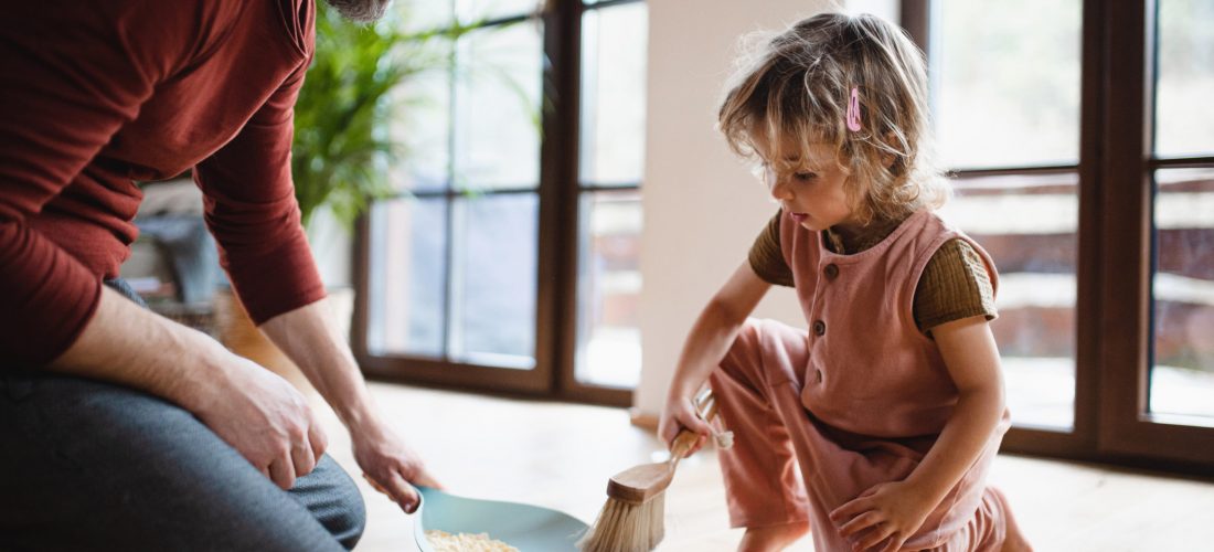 Mid adult father with a small daughter sweeping cornflakes at home, daily chores concept.