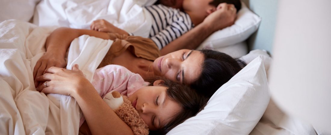 Mid adult parents sleeping in bed with their two young children, waist up, close up