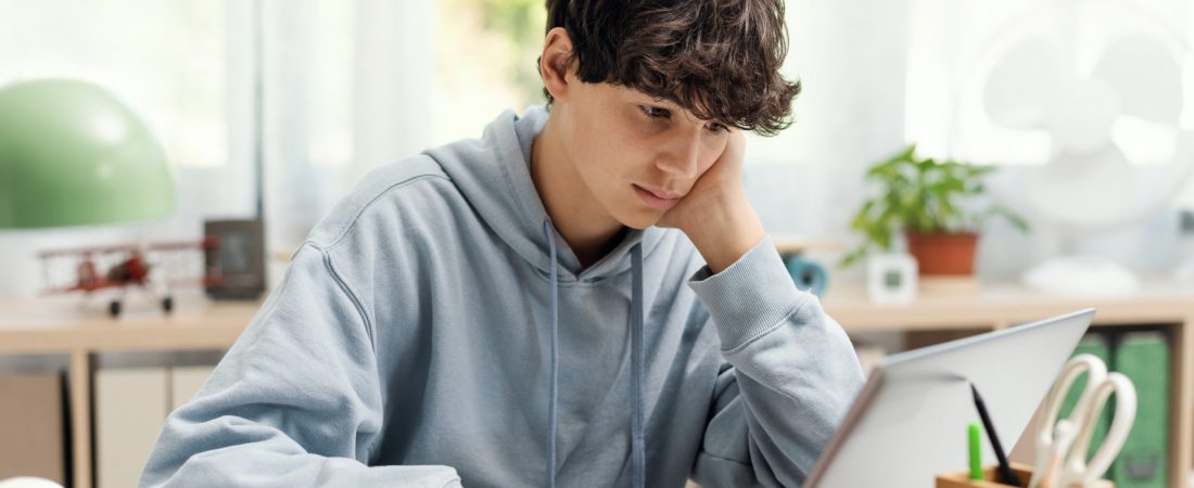 Academic student sitting at desk at home and connecting online using his laptop, technology and online learning concept